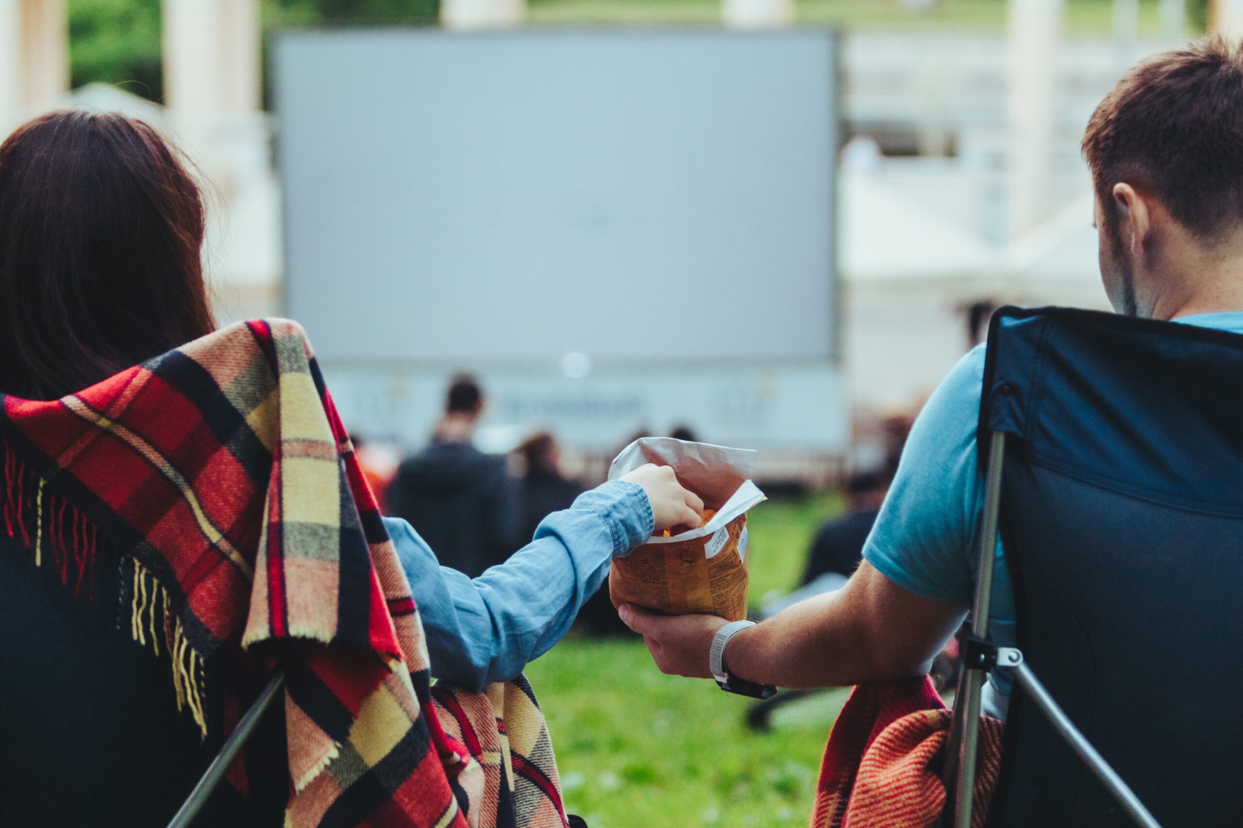 couple sitting in camp-chairs in city park looking movie outdoors at open air cinema lifestyle