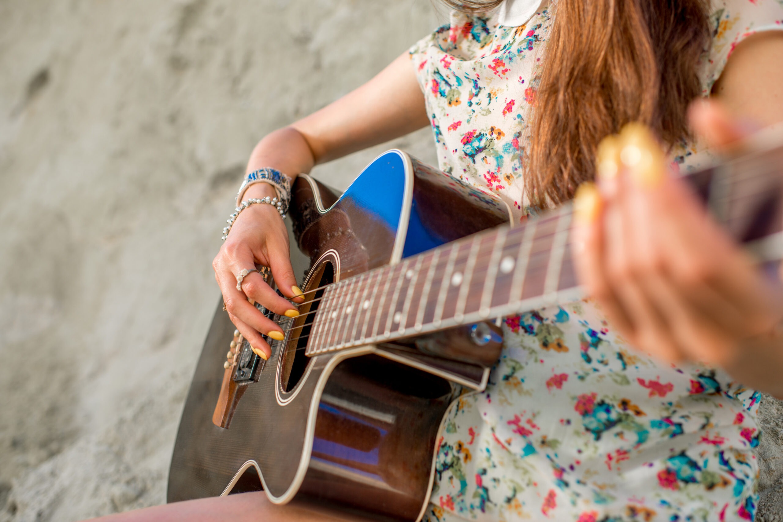 Young woman playing acoustic guitar sitting on the sand